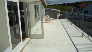 A balcony with a glass door, lounge chairs, and a view of a hilly landscape. - Hotel Eyjar (Vestmannaeyjar)