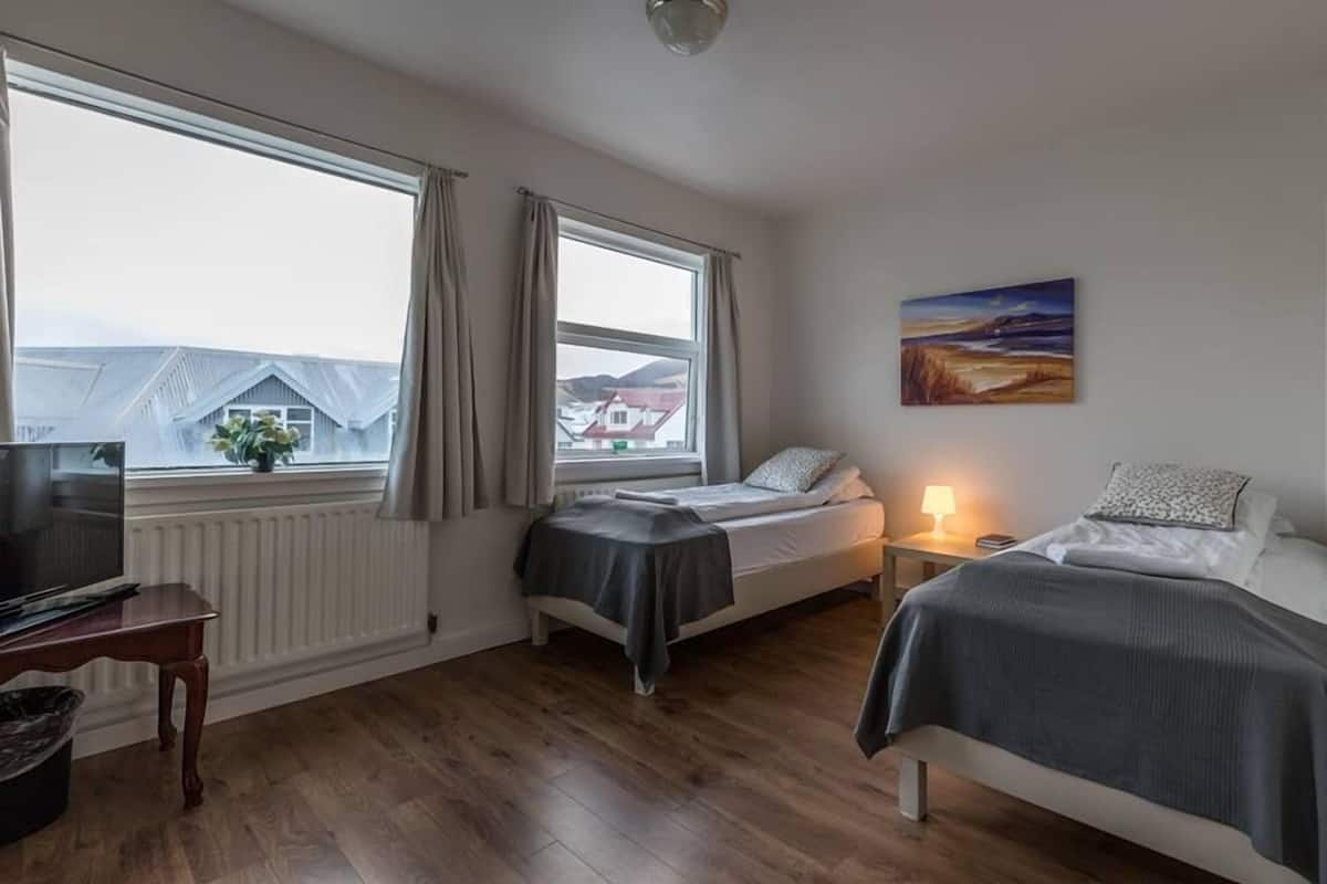 Un dormitorio con dos camas individuales, un televisor, un escritorio y una ventana con cortinas.