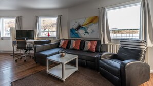 A modern living room with a black leather sofa, a white coffee table, a TV, and a large abstract painting. - Hotel Eyjar (Vestmannaeyjar)