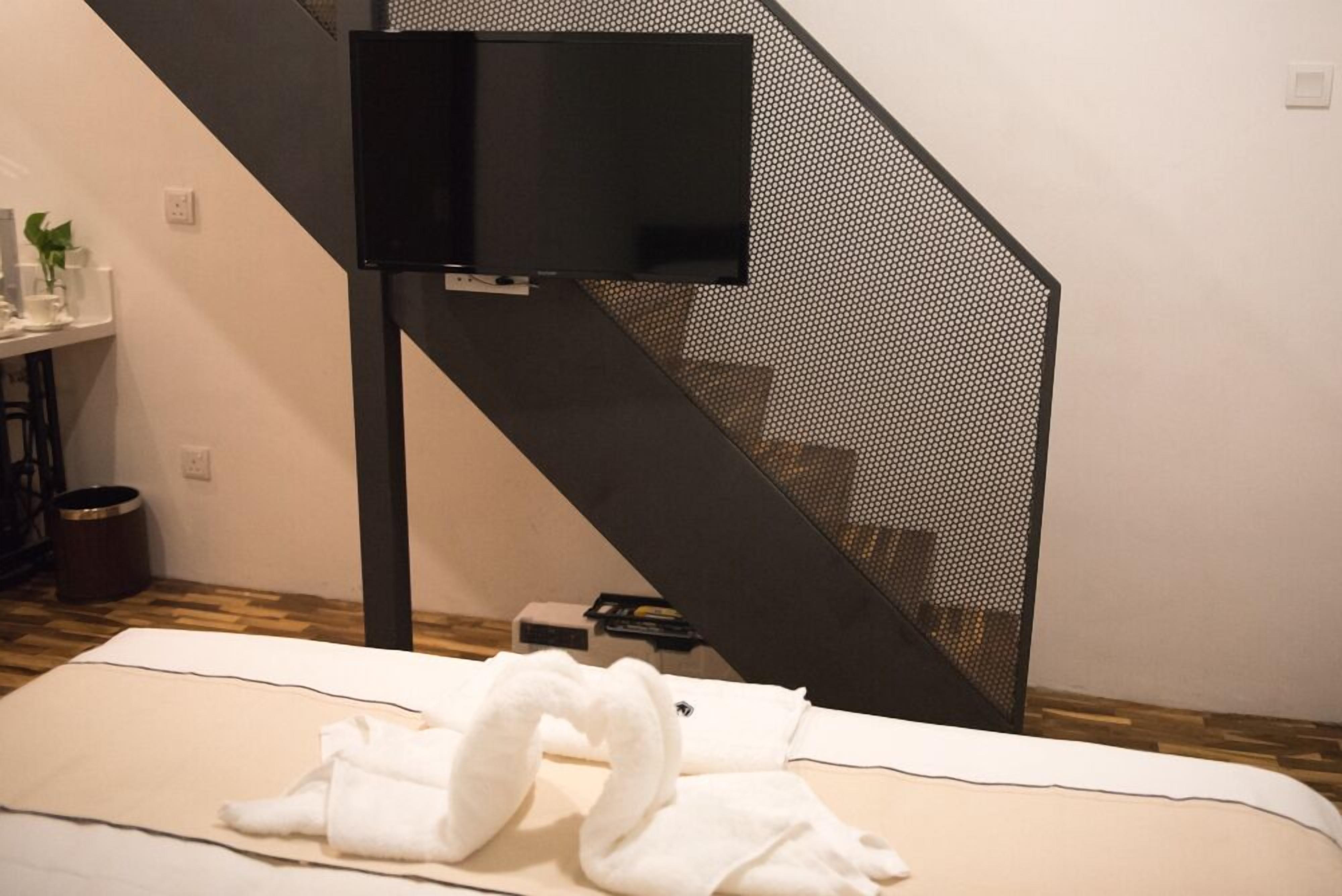 A room with a bed, a TV mounted on a black stand, and a staircase with a mesh design.