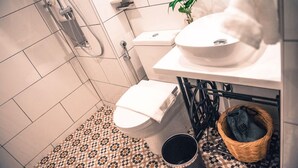 Un baño con inodoro blanco, lavamanos, ducha y suelo estampado.