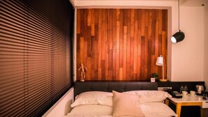 Un dormitorio moderno con un panel de madera en la pared, una cama con ropa de cama blanca, una mesita de noche con una lámpara y una planta pequeña.