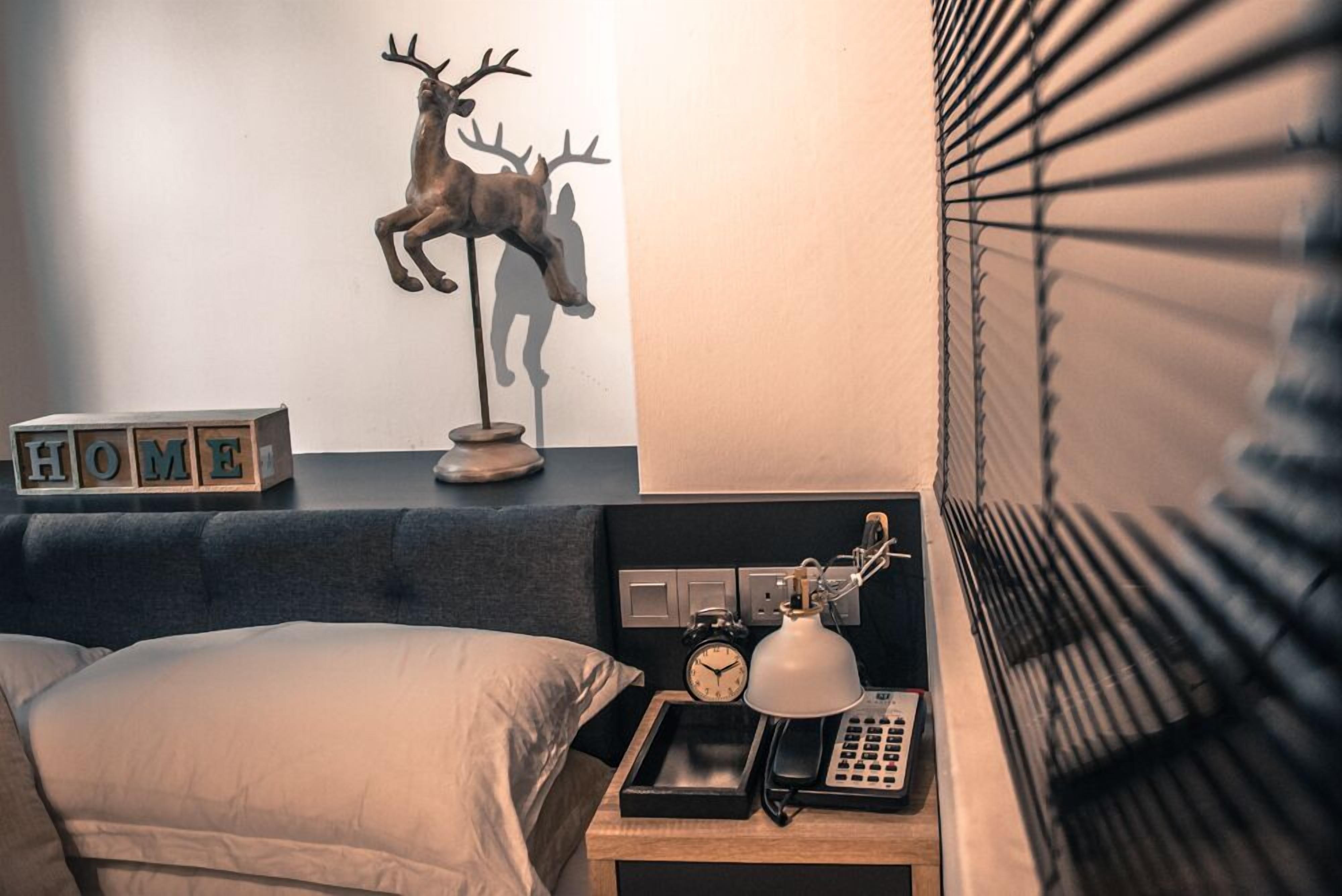 A bedroom with a bed, bedside table, lamp, clock, and a decorative deer sculpture.