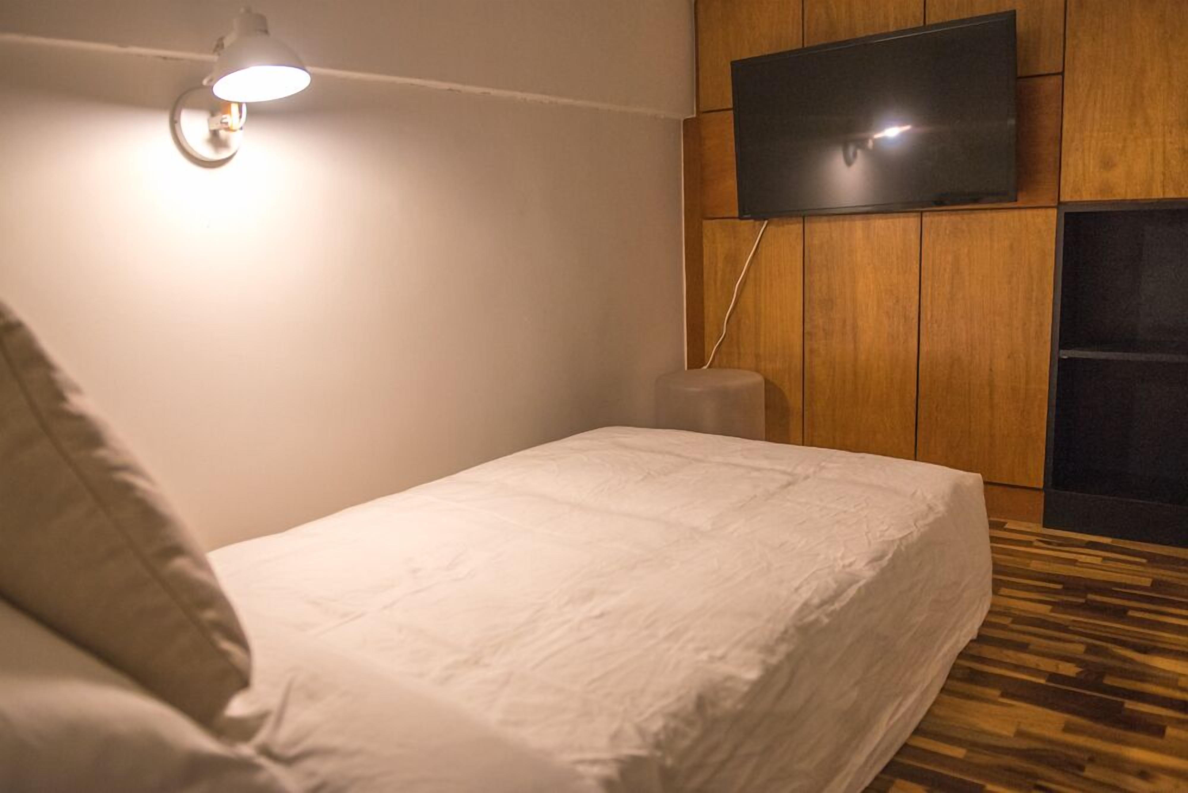 Un dormitorio con cama, televisor montado en la pared y suelo de madera.