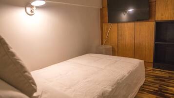 Un dormitorio con cama, televisor montado en la pared y suelo de madera.