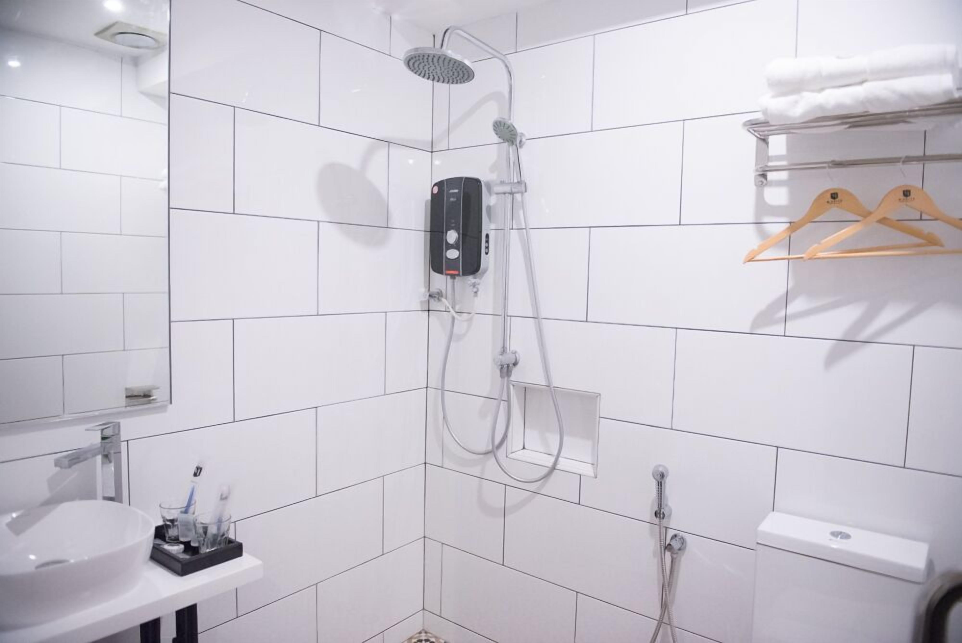 A modern bathroom with white tiles, a built-in sink, a handheld showerhead, and a towel rack.