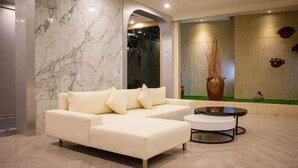 A modern living room with a white sectional sofa, a round coffee table, and a marble wall. - OHYA Chain Boutique Motel-Taoyuan  (Taoyuan City)