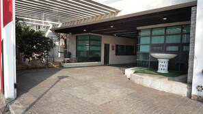 Una entrada de edificio con porche cubierto, ventanas amplias y una jardinera decorativa.