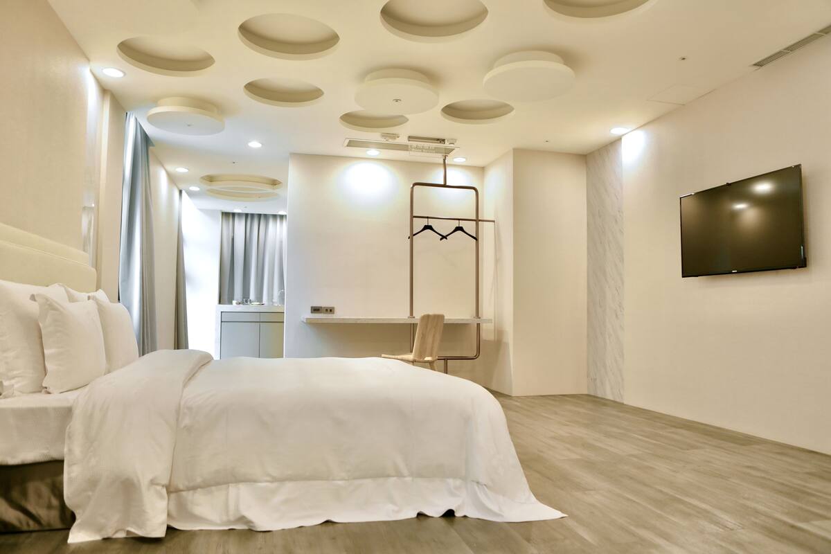 Une chambre d’hôtel moderne, dotée d’un grand lit, d’un téléviseur fixé au mur et d’un design minimaliste.