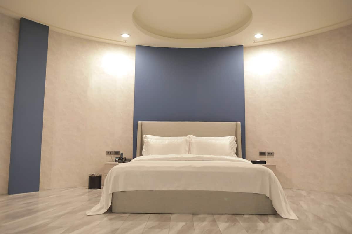 A modern bedroom with a large bed, a nightstand, and a wall-mounted light fixture.