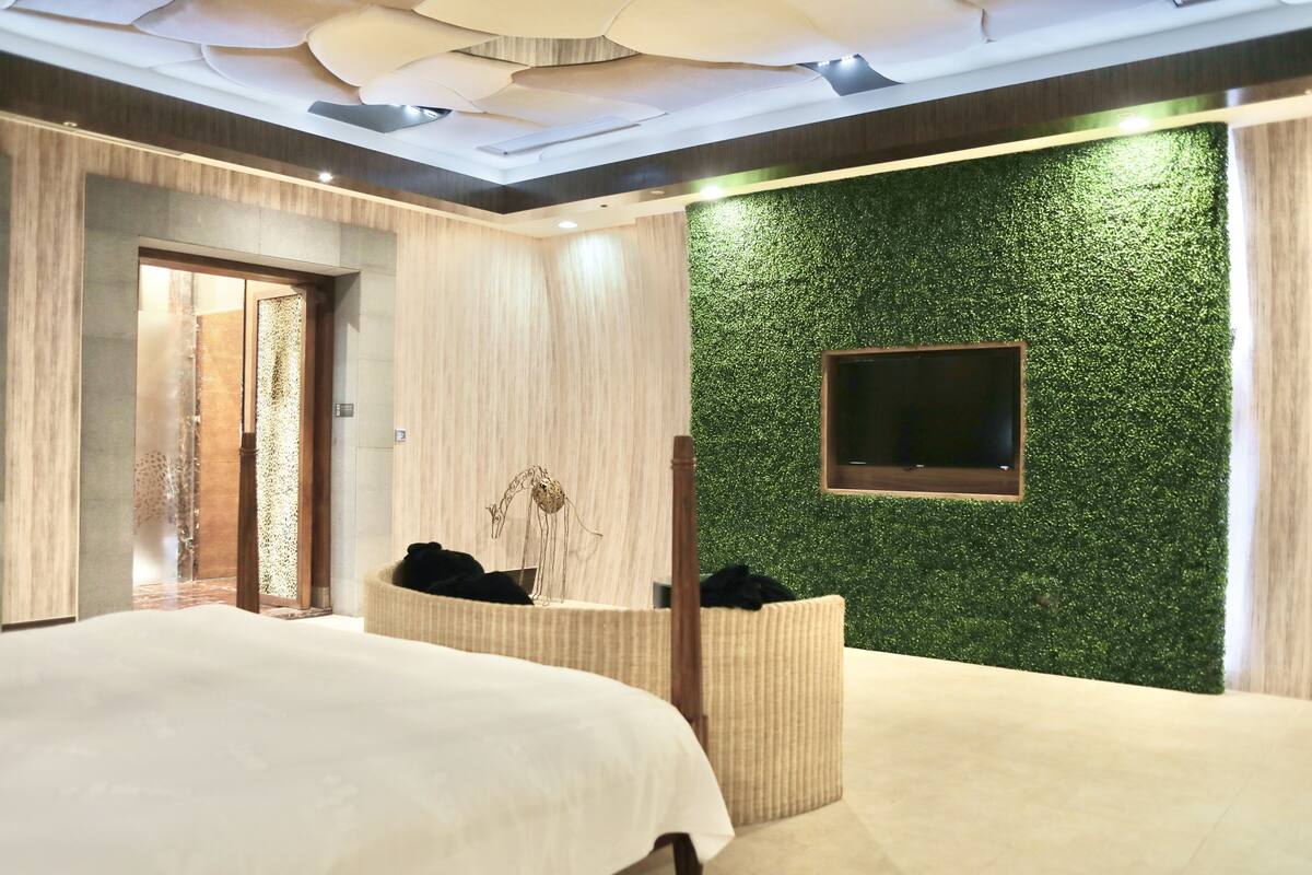Une chambre d’hôtel moderne dotée d’un grand lit, d’un petit coin salon, d’un téléviseur fixé au mur et d’un mur texturé de couleur verte.