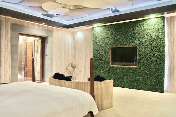 Una habitación de hotel moderna con una cama grande, un pequeño rincón de descanso, un televisor montado en la pared y una pared verde con textura.