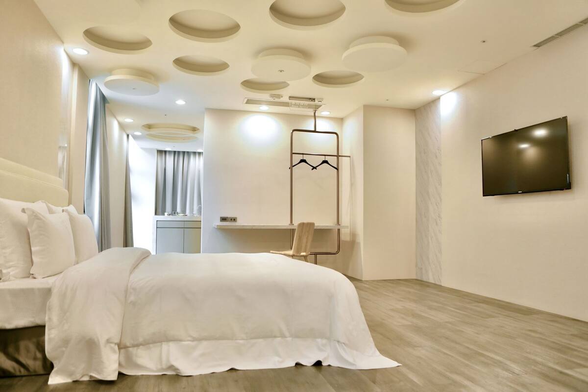 Une chambre d’hôtel moderne avec un lit, une télévision, un porte-manteau et une salle de bain à l’arrière-plan.