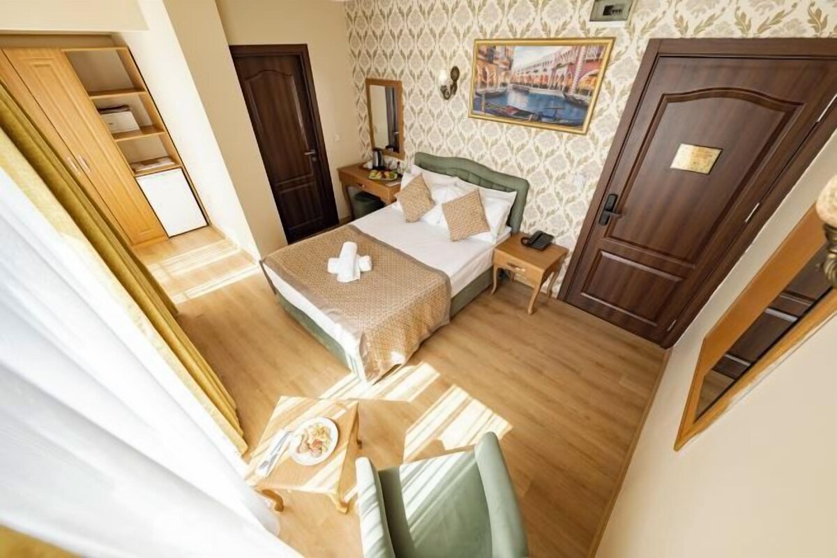 A hotel room with a bed, bedside table, and a view of a cityscape through the window.