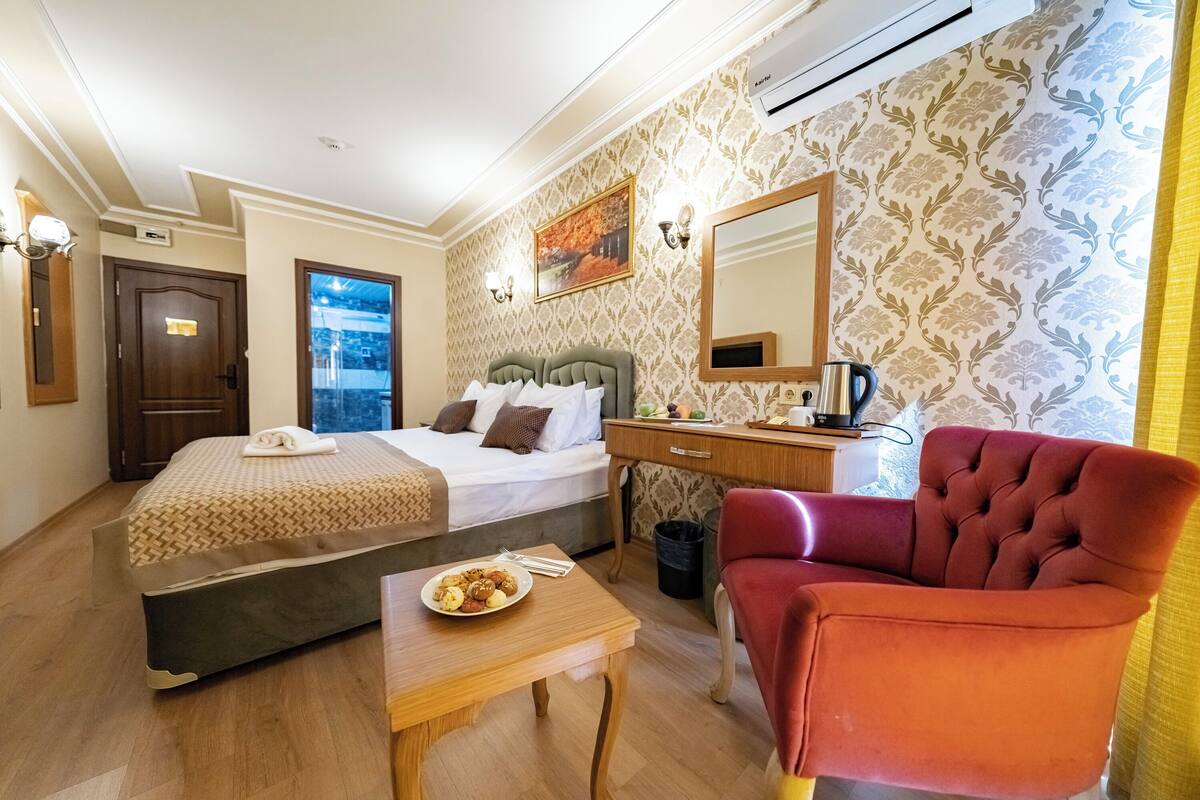 Habitació d'hotel amb llit, escriptori, cadira, taula petita amb menjar i finestra.