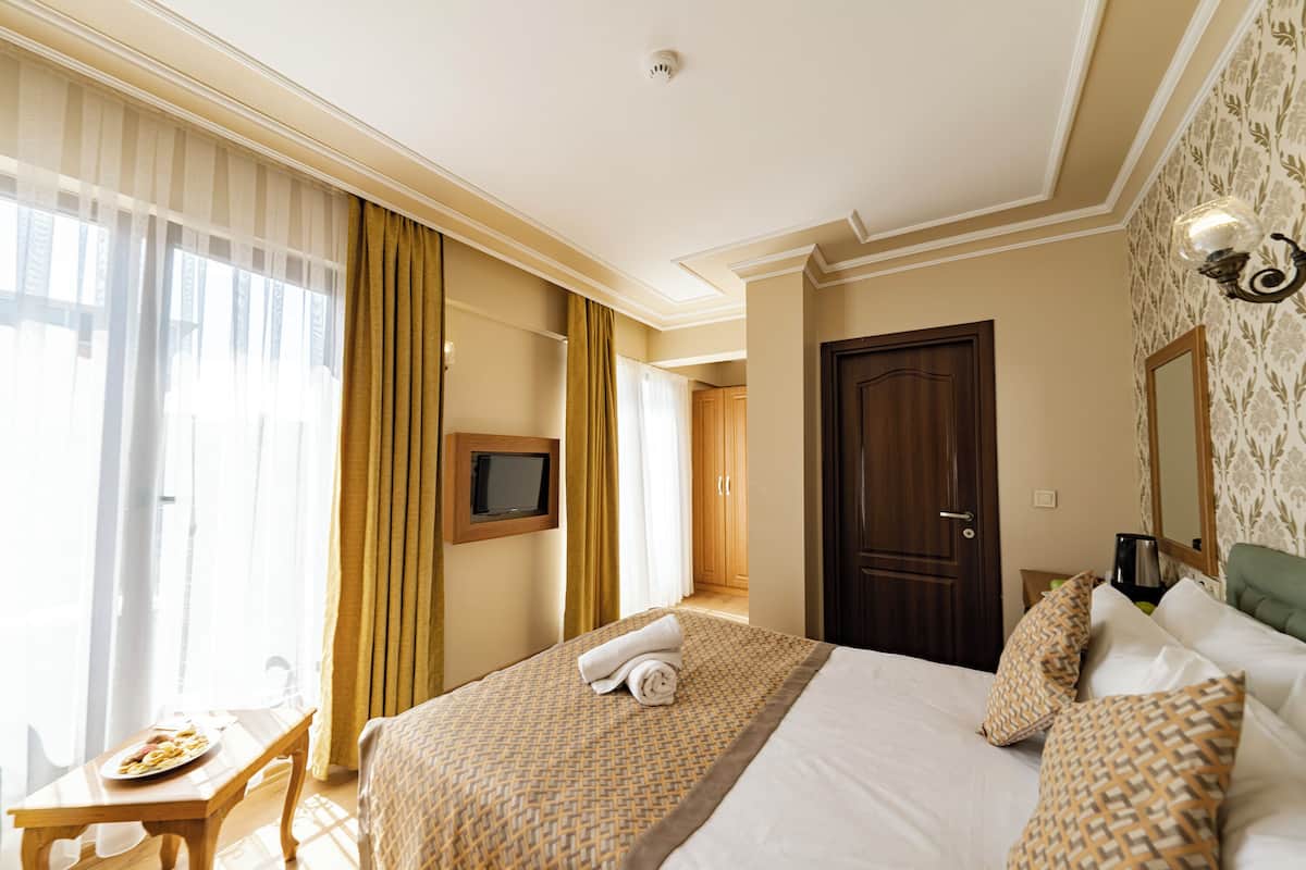 Una habitació d'hotel amb un llit ben fet, una televisió penjada a la paret, una taula de menjador amb un plat de menjar i una finestra amb cortines.