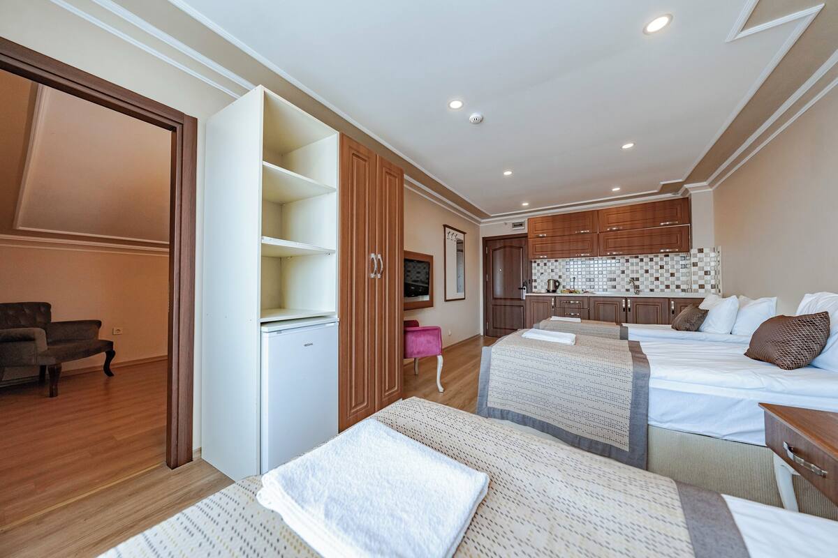 Habitació d'hotel amb dos llits, una cuineta, zona de seients i un armari.