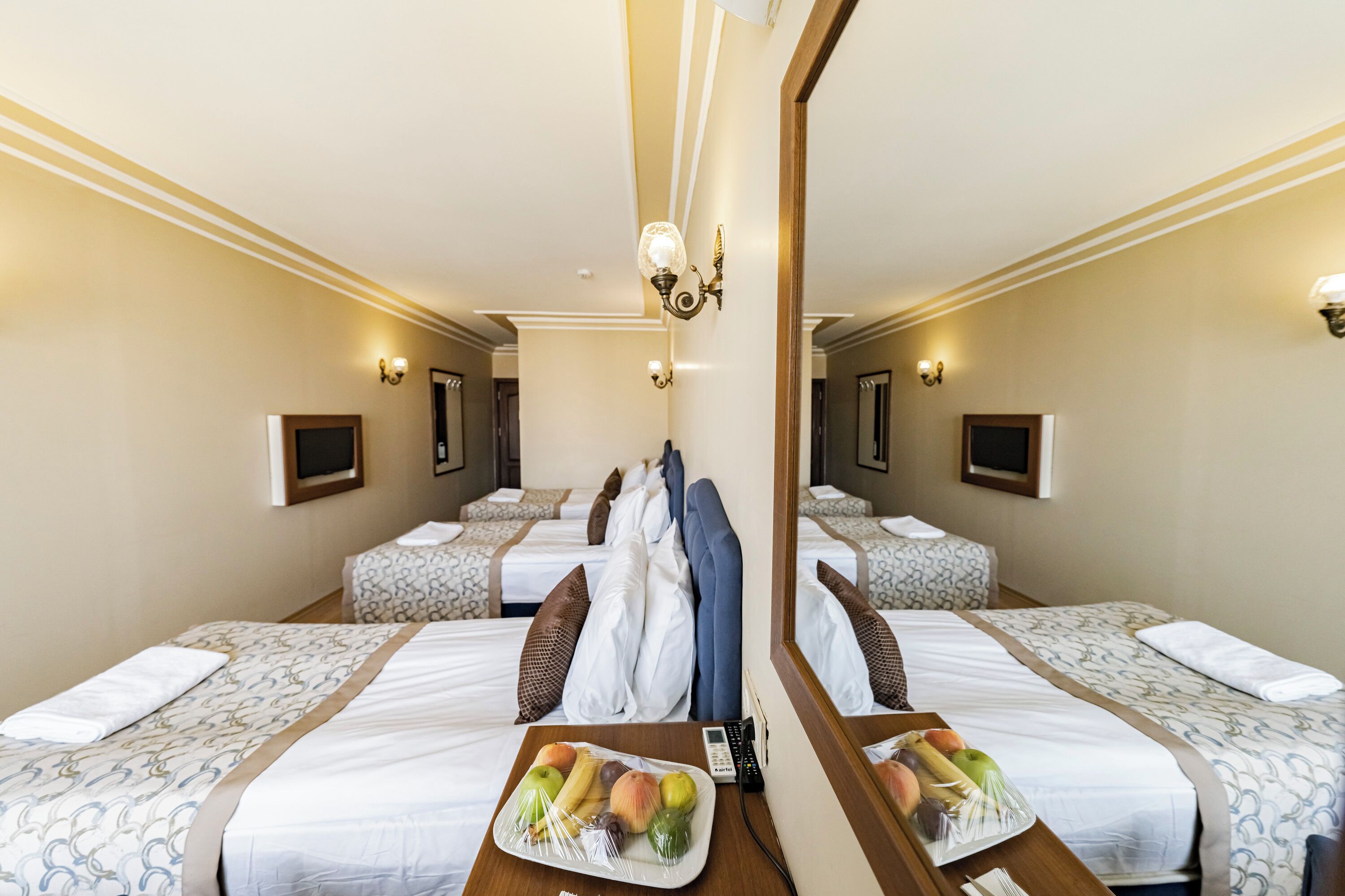 Habitación de hotel con dos camas, un espejo, una mesita de noche con fruta y un teléfono.