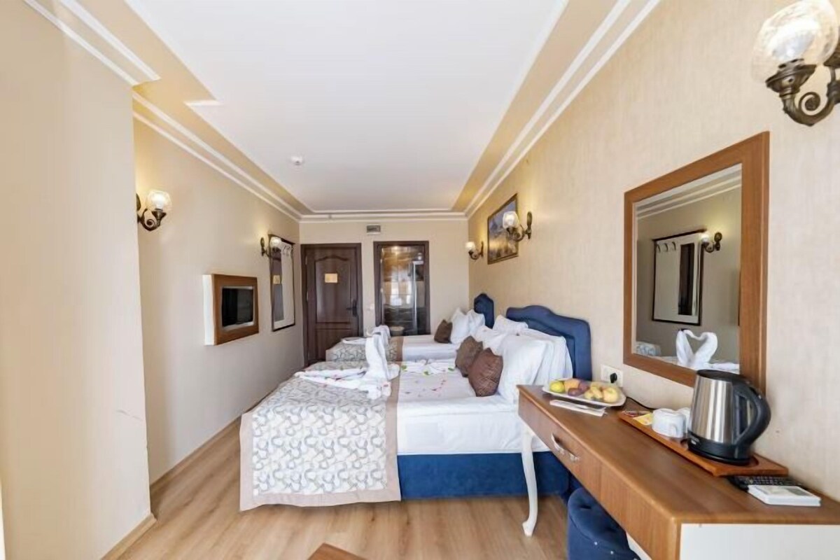 A hotel room with two beds, a desk with a kettle, and a mirror.