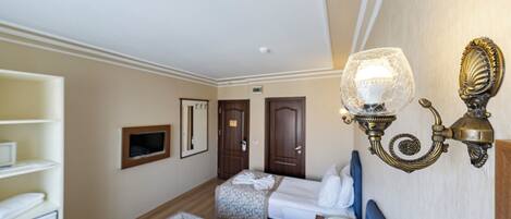 A hotel room with two beds, a wardrobe, a desk, and a wall-mounted light fixture.