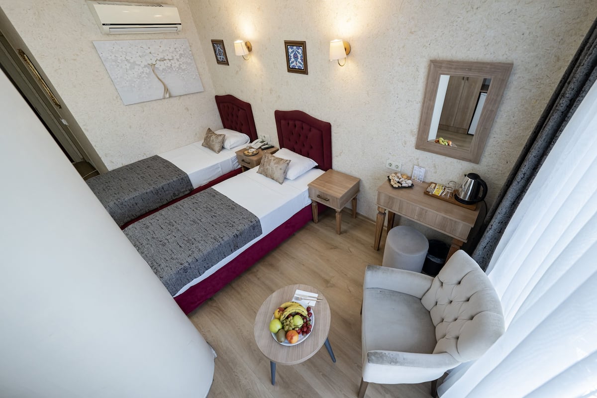 A hotel room with two beds, a small table with fruit, a chair, a desk with a mirror, and wall-mounted lights.