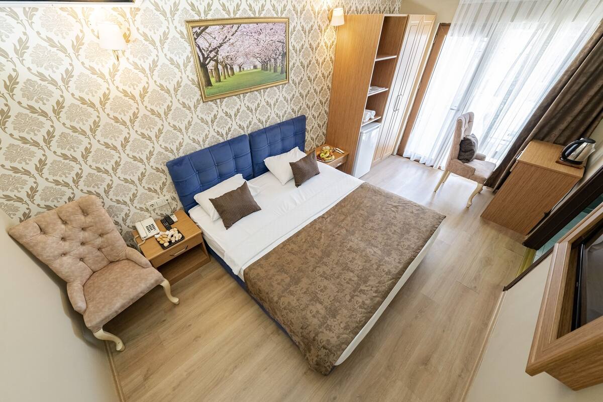 A bedroom with a large bed, a wooden nightstand, a chair, a wardrobe, and a painting on the wall.