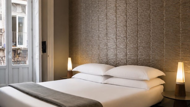 Una camera d'albergo moderna con un letto grande, un muro strutturato, un pavimento in legno e un lampadario.
