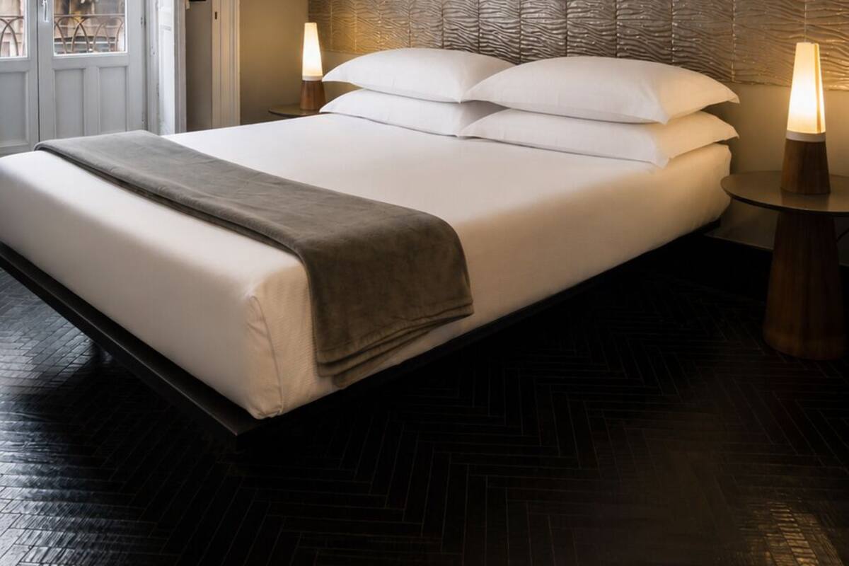 Ein modernes Hotelzimmer mit einem großen Bett, einer strukturierten Wand, einem Holzboden und einer Kandelaber.