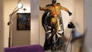 Una stanza con un divano viola, un tavolino, un quadro astratto di grandi dimensioni e una statua.