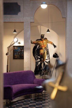 Una habitación con un sofá morado, una mesita, un cuadro abstracto grande y una estatua.