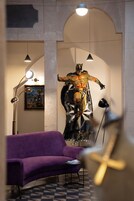 Una stanza con un divano viola, un tavolino, un quadro astratto di grandi dimensioni e una statua.