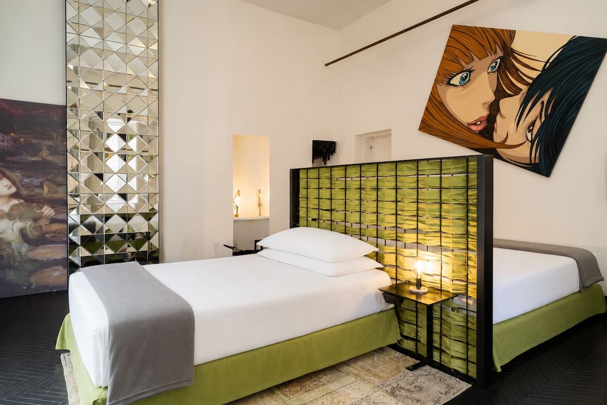 Ein Hotelzimmer mit einem Bett, einem Nachttisch, einer Wandlampe, einer dekorativen Wandverkleidung und einem großen Gemälde.