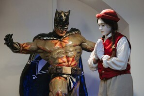 Een persoon in een kostuum met een cape en een andere persoon in een rode hoed en wit shirt.