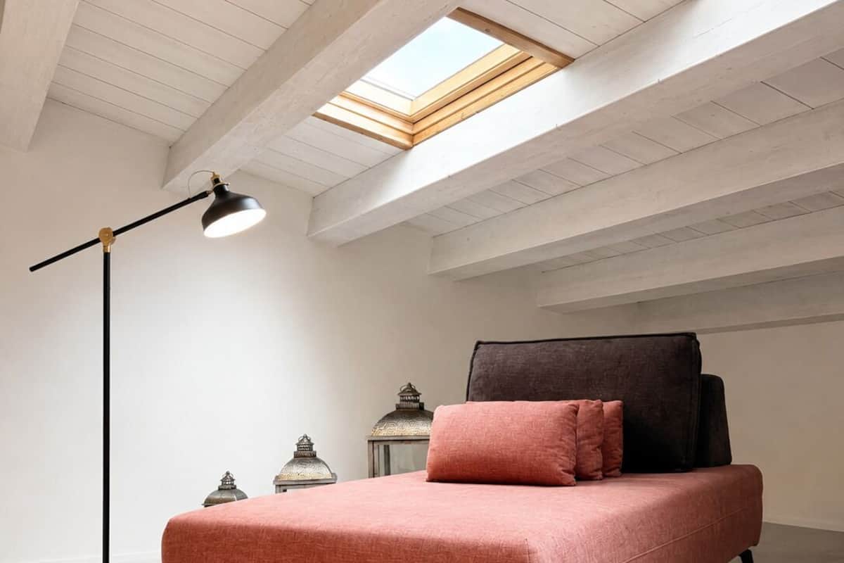 Ein Schlafzimmer mit einem Bett, einer Stehlampe und Dachfenstern.
