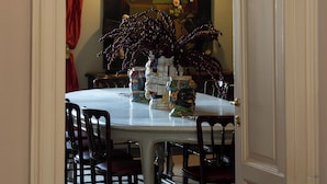 Una sala da pranzo con tavolo bianco, sedie scure, un lampadario e un quadro appeso al muro.