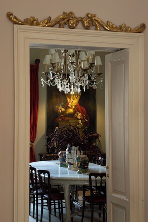 Comedor con una mesa blanca, sillas oscuras, una araña y un cuadro en la pared.