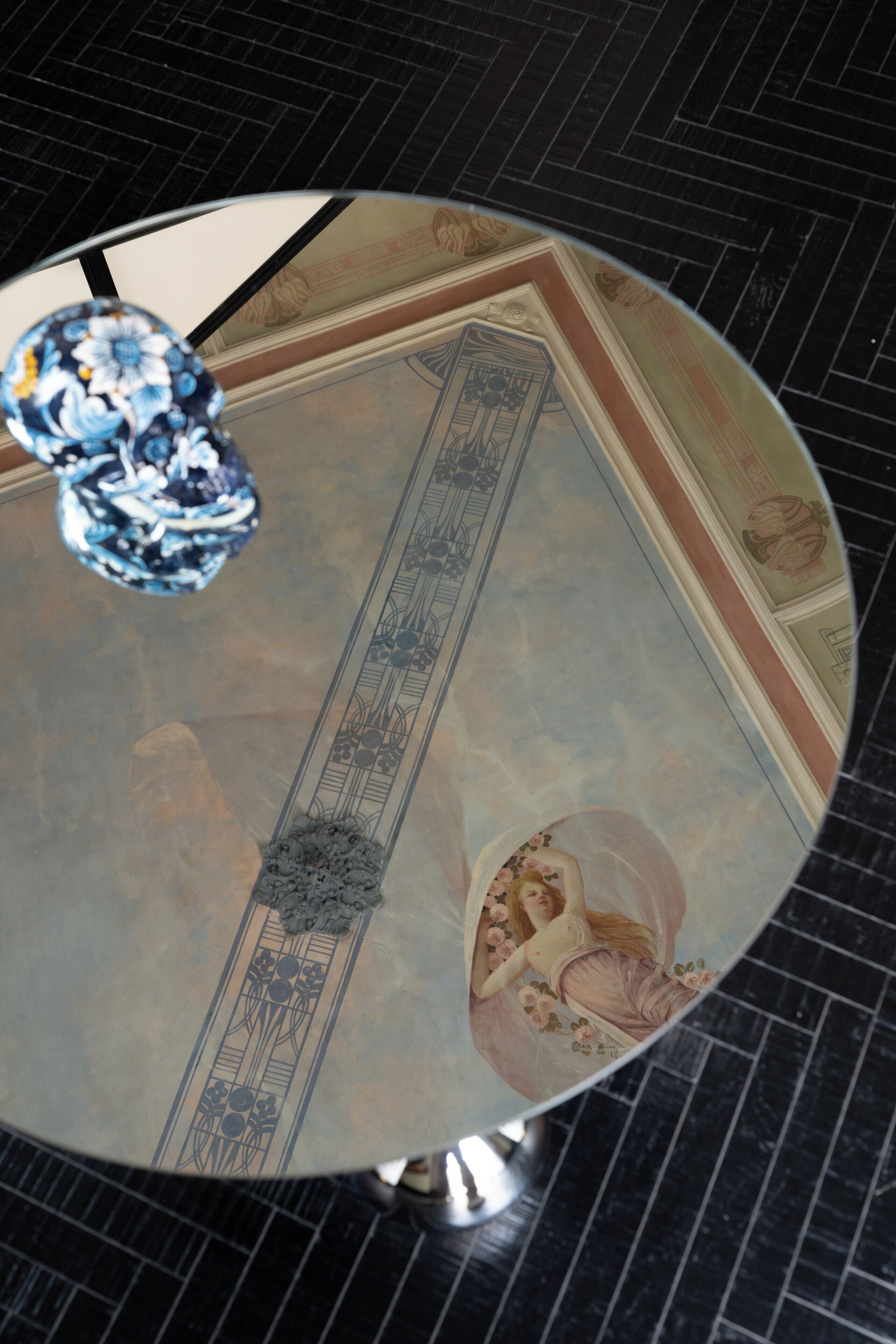 A round table with a glass top, a decorative mirror, and a floral design on the wall.