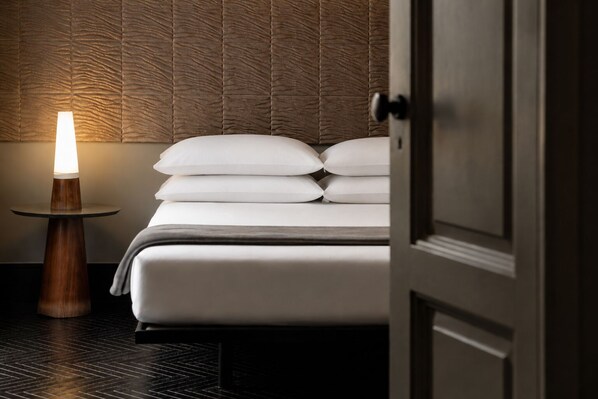 A hotel room with a bed, pillows, a bedside table with a lamp, and a textured wall. - Asmundo di Gisira (Catania)