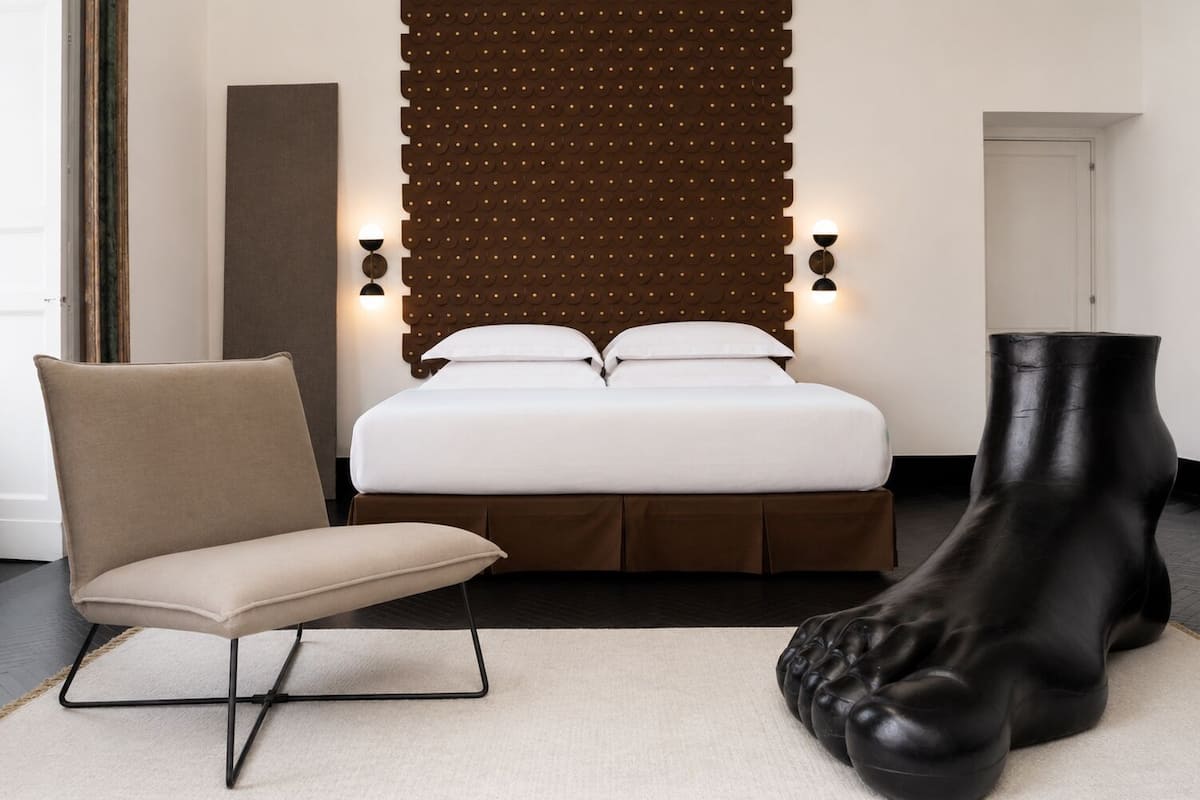 Ein modernes Hotelzimmer mit einem Bett, einem Sessel und einer markanten, schwarzen Skulptur.