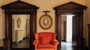 A room with a large wooden chair, a framed portrait, and a chandelier.