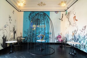 A dining area with round tables, chairs, and a mural with abstract designs. - Asmundo di Gisira (Catania)