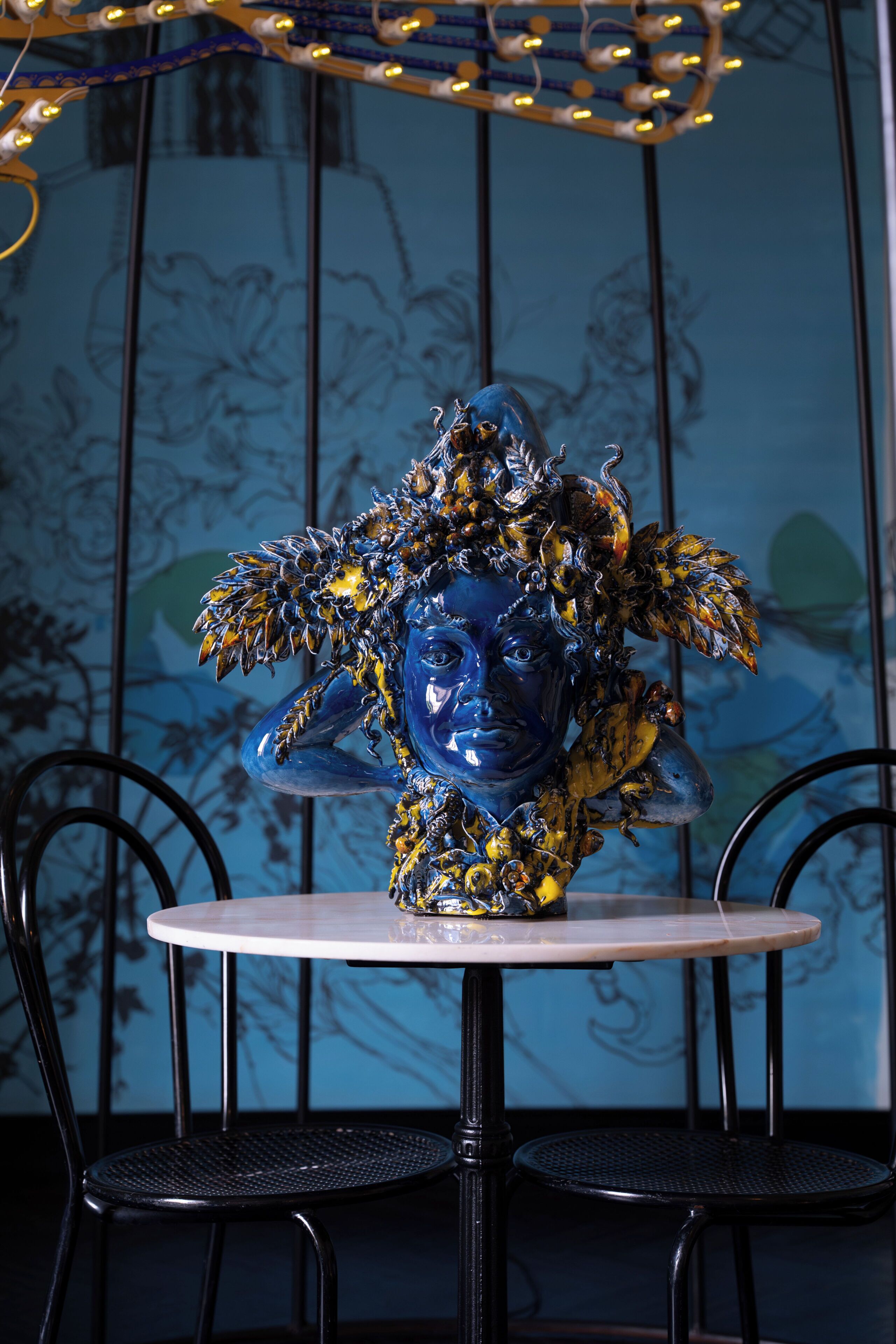 A blue ceramic sculpture on a round table with black chairs.