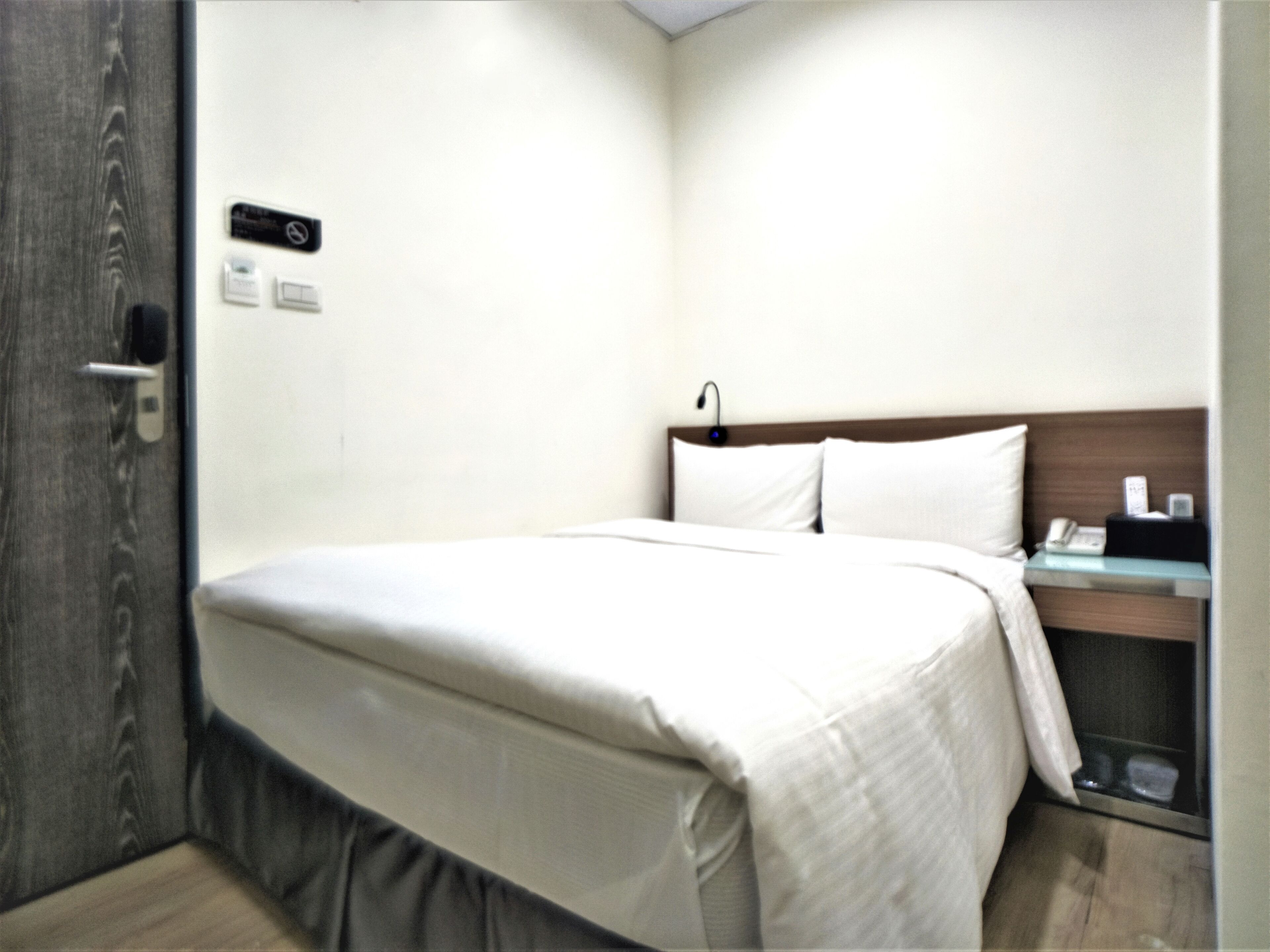 A hotel room with a bed, bedside table, and a door.