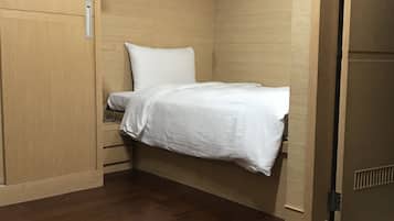A small, compact room with a bed, wooden wardrobe, and a door.