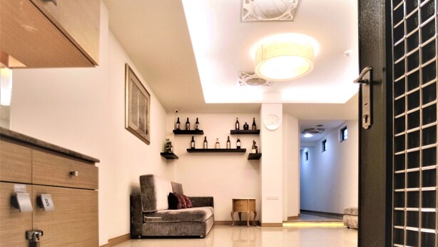 A hotel lobby with a wooden cabinet, a grey sofa, and wine bottles on shelves. - West 59 Inn  (Taipei)