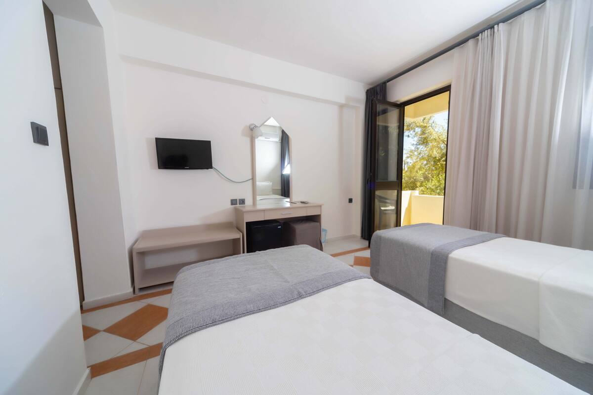 A hotel room with two beds, a desk, a TV, and a window with curtains.