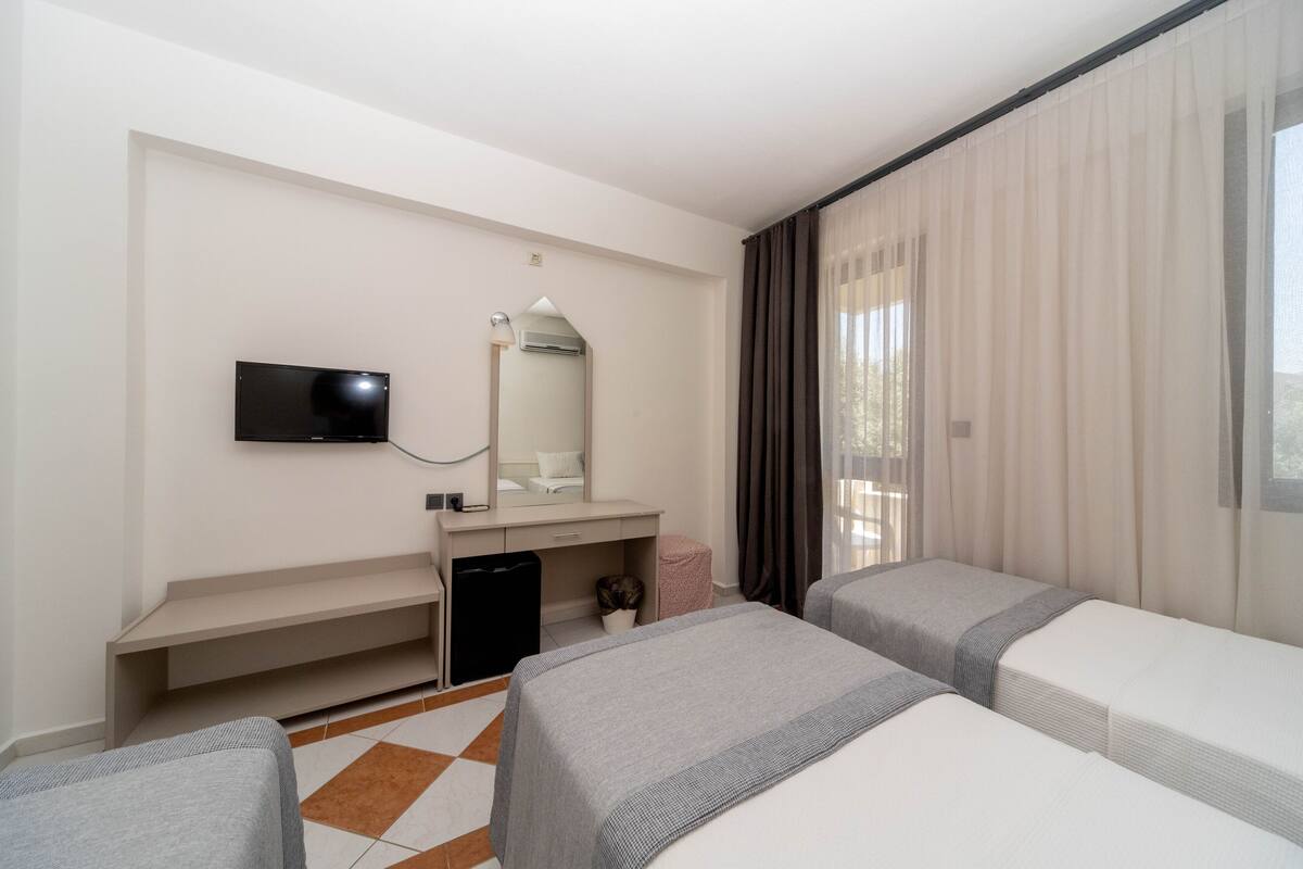 A hotel room with two beds, a desk with a TV, a mirror, and a window with curtains.