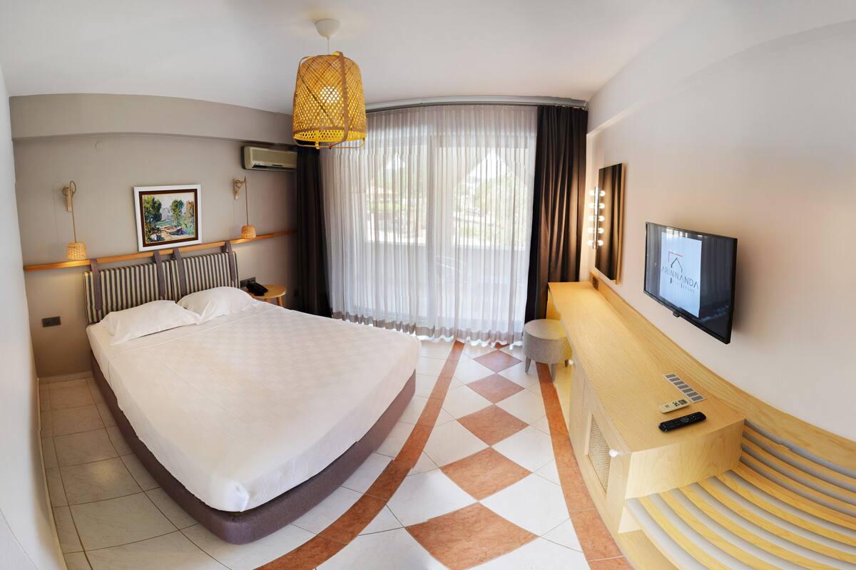 A hotel room with a large bed, a desk with a TV, a chair, and a window with curtains.
