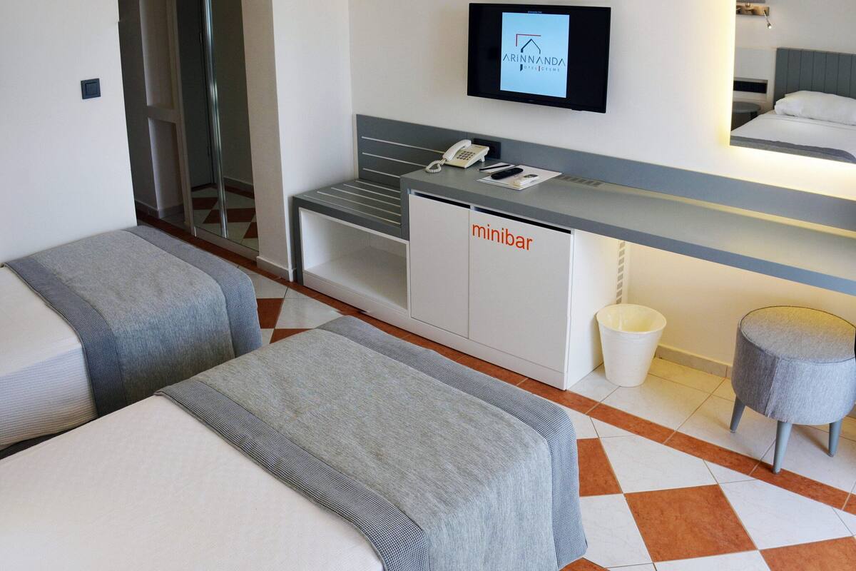 A hotel room with two beds, a desk with a telephone, a television, and a minibar.