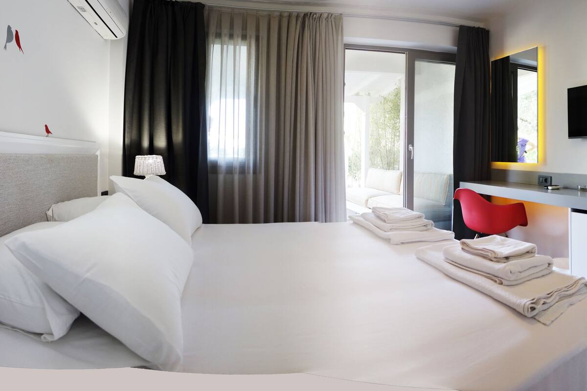 A hotel room with a large bed, a desk with a chair, a TV, and a window with curtains.